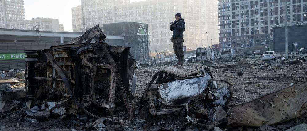 Ein Mann steht auf einem Autowrack inmitten der Zerstörung, die nach dem Beschuss eines Einkaufszentrums in Kiew entstanden ist.