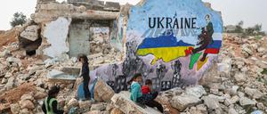 Kinder im syrischen Binnish neben einem Wandgemälde, das aus Solidarität mit der Ukraine an die Wand eines zerstörten Hauses gemalt wurde. Russlands Bombardements haben in Syrien viele Ortschaften zerstört.