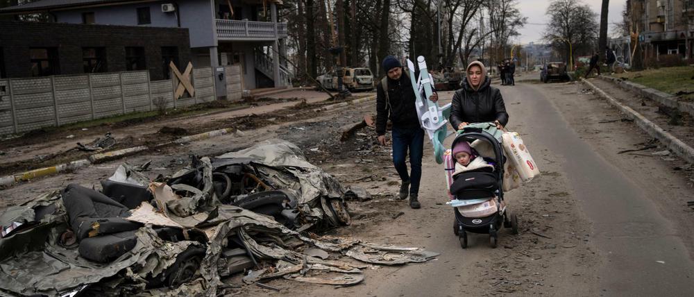 Eine Familie geht an einem durch russische Panzer zerstörtem Auto in Butscha vorbei.