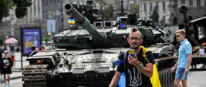 Ein Mann in einem T-Shirt mit dem Symbol des ukrainischen Wappens und der ukrainischen Flagge telefoniert in der Nähe der zerstörten Ausrüstung der russischen Armee in Kiew.