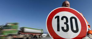 Ein Straßenwärter hält an der Autobahn ein Schild mit der Aufschrift "130" in den Händen.