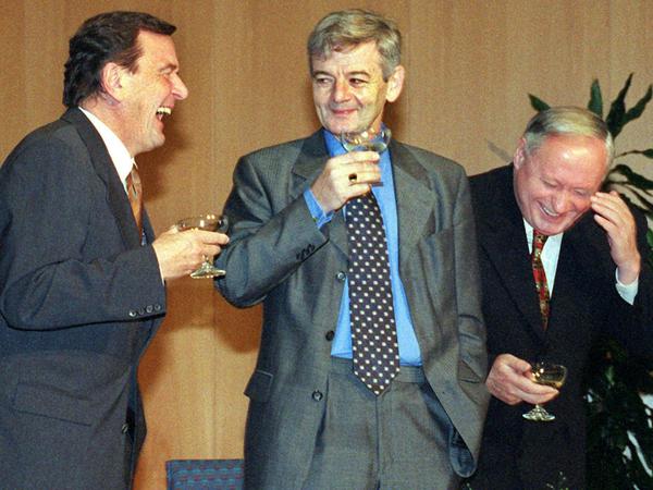 Lachend und mit einer Sektschale in der Hand unterhalten sich Gerhard Schröder (l-r), Joschka Fischer und Oskar Lafonatine nach der Unterzeichnung des rot-grünen Koalitionsvertrages in Bonn (Archivfoto vom 20.10.1998).