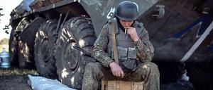 Soldat vor Panzer auf Kiste mit Zigarette, schaut nach unten