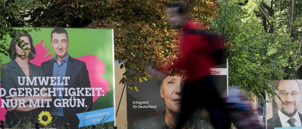 Ein Passant geht am 18.09.2017 in Berlin an Wahlplakaten mit dem Porträt der Grünen-Spitzenkandidaten Katrin Göring-Eckardt und Cem Özdemir, Bundeskanzlerin Merkel (CDU) und dem SPD-Parteivorsitzenden Martin Schulz vorbei. 