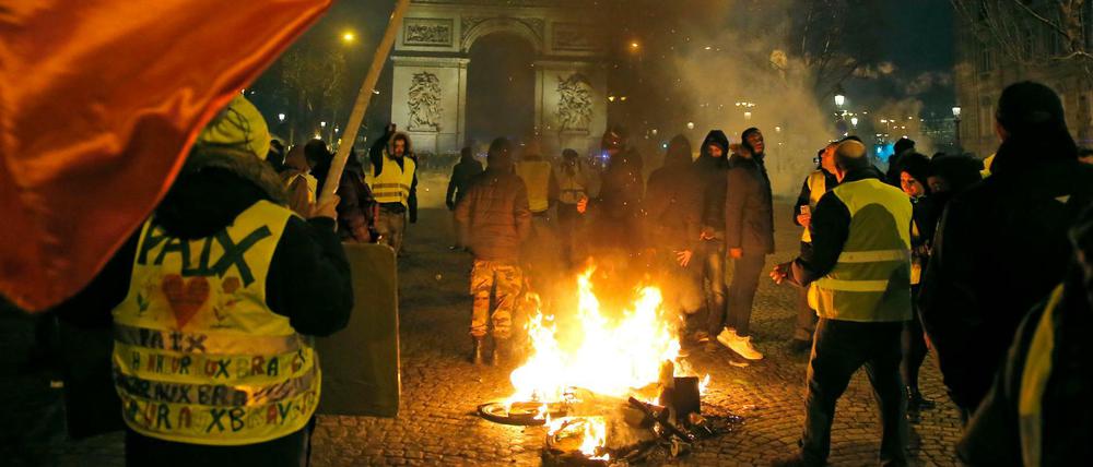 Demonstranten mit gelben Westen stehen neben einem brennenden Fahrrad auf den Champs-Elysées. 