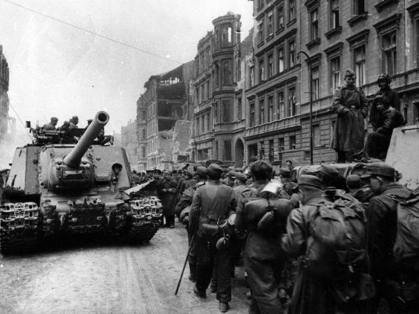 Deutsche Gefangene marschieren bei Kriegsende in Berlin an einem Panzer und sowjetischen Soldaten vorbei.