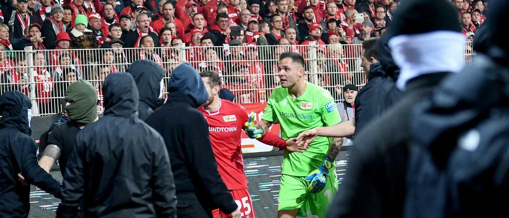 Unions Christopher Lenz und Rafal Gikiewicz beruhigen vermummte Fans ihres Vereins nachdem die Hertha-Fans Pyrotechnik auf das Spielfeld schießen.