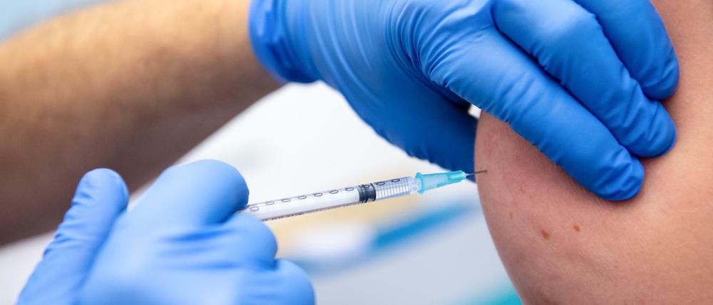 Impfung im Oberarm mit Spritze in Hand mit blauem Handschuh.