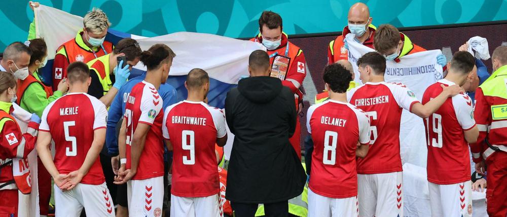 Die dänischen Spieler stehen zusammen, während Christian Eriksen auf dem Rasen behandelt wird. 