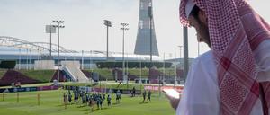 Ein Mann schaut in Doha auf sein Handy, während die Fußballer von Bayern München trainieren.