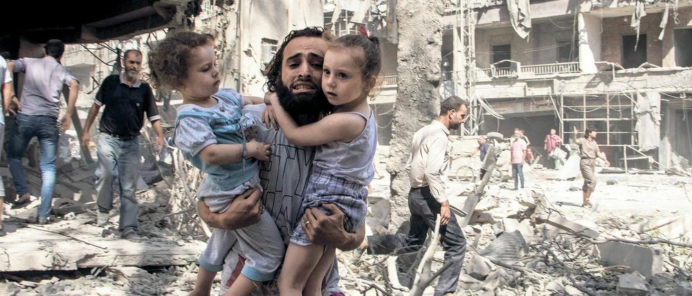 Ein Syrer trägt seine beiden Töchter durch die Ruinen von Aleppo. 