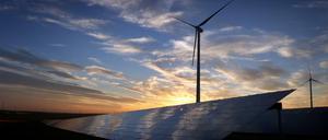 Windräder stehen hinter den Solarzellen einer Solarkraftanlage in Bayern. 