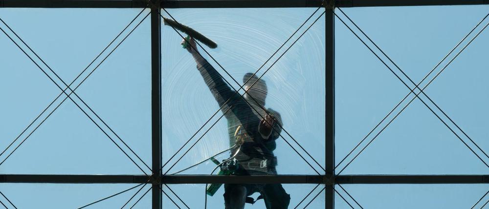 Ein Gebäudereiniger putzt in 27 Meter höhe ein gläsernes Dach.