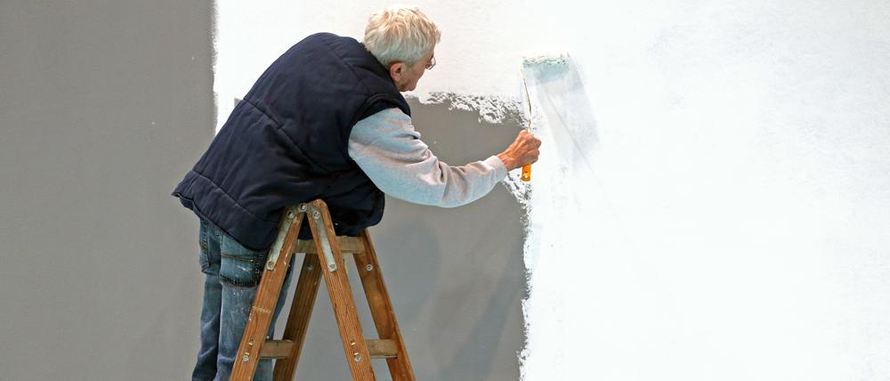 Ein älterer Herr mit grauen Haaren weißt eine Wand.