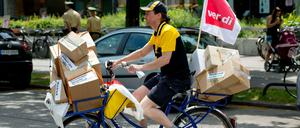 Ein Mitarbeiter der Deutschen Post fährt in München mit einem symbolisch überladenen Postfahrrad über die Straße.