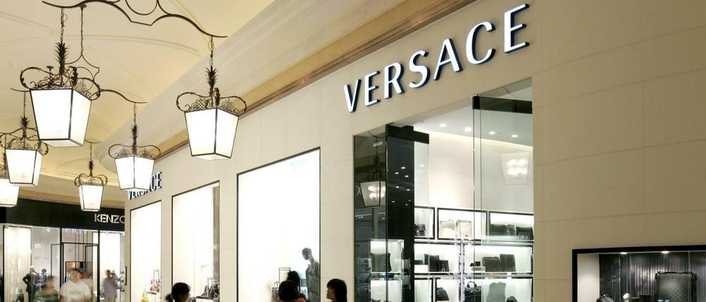Besucher gehen vor einem Versace-Shop in einem Luxus-Einkaufszentrum in Macao in China.