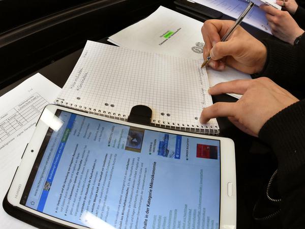 Ein Student schreibt im Hörsaal eine Vorlesung mit, neben seinem Collegeblock lieg ein Tablet-Computer.