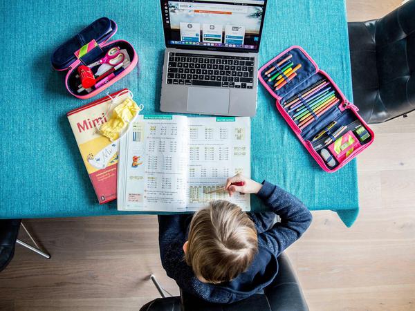 Ein Kind rechnet in seinem Schulbuch Matheaufgaben, vor ihm steht ein Laptop.