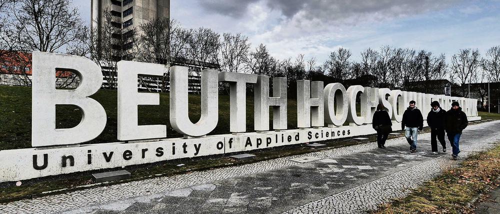 Vier Studierende gehen einen gepflasterten Weg entlang, parallel dazu ist der überdimensionale Schriftzug Beuth Hochschule zu sehen.