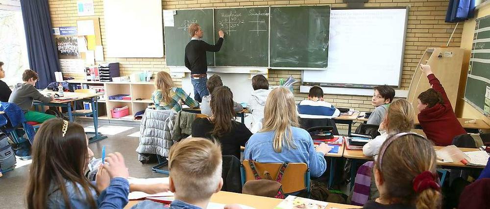 Ein Lehrer steht mit dem Rücken zur Klasse und schreibt Matheaufgaben an die Tafel.