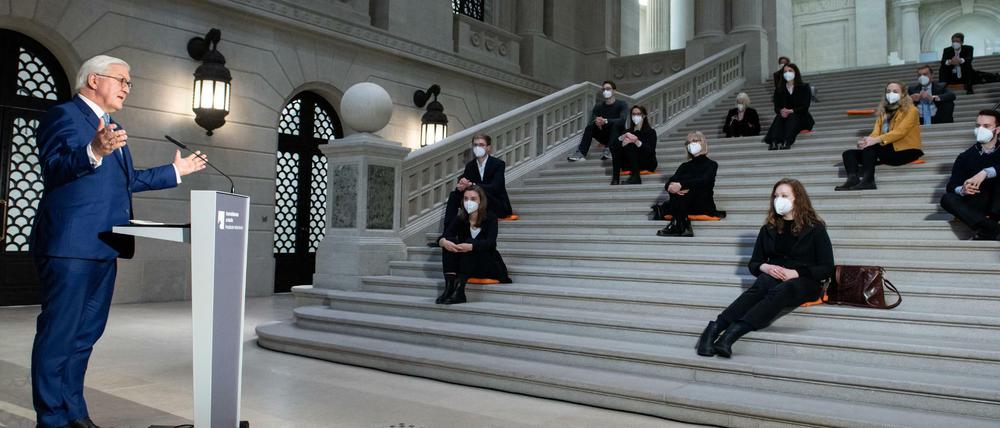 Steinmeier steht an einem Rednerpult, Studierende sitzen mit Abstand voneinander auf einer Freitreppe.