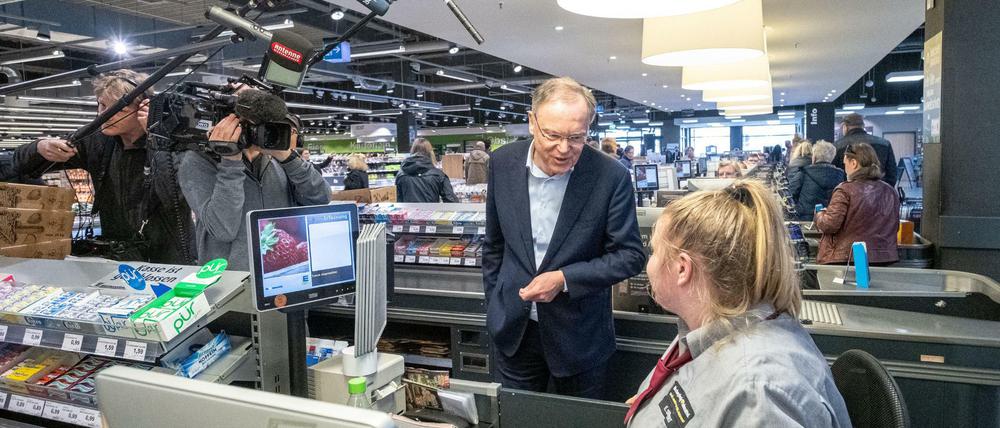 Ein Politiker im Gespräch mit einer Kassiererin im Supermarkt, in Begleitung eines Filmteams.