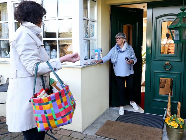 Eine jüngere Frau bringt einer Älteren einen Einkaufskorb mit Lebensmitteln an die Haustür.