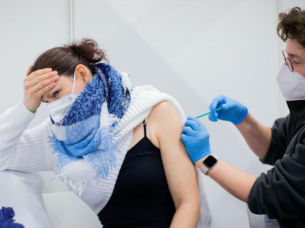 Eine junge Frau wendet sich ab und hält sich den Kopf, während sie eine Impfung von einer Ärztin erhält.