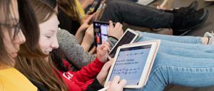 Schülerinnen sitzen mit ihren iPads auf dem Boden und lösen Matheaufgaben.