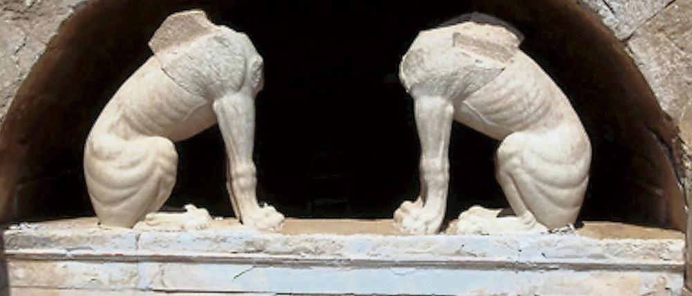 Zwei kopflose Sphinxen stehen in einer Ausgrabungsstätte unter einem Torbogen auf einem Sockel.