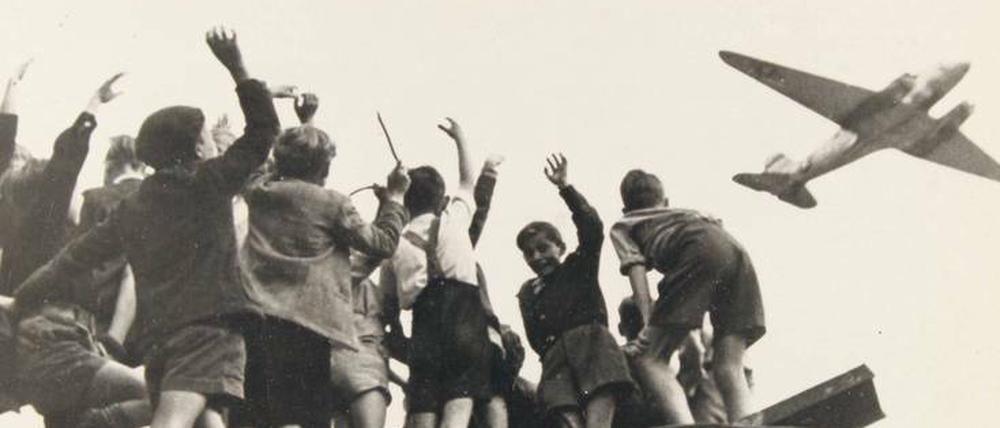 Rettung aus der Luft: Kinder winken im Juli 1948 am Flughafen Tempelhof einem „Rosinenbomber“ zu. Mit der Luftbrücke versorgten die Westalliierten während der Berlin-Blockade die Bevölkerung mit Lebens- mitteln und lebenswichtigen Hilfsmitteln wie Brennmaterial.