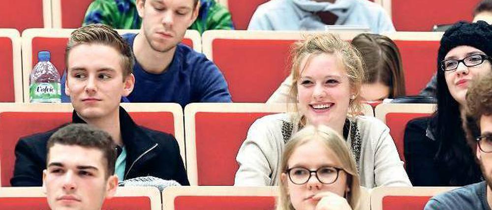 Junge Studierende sitzen lächelnd in einem Hörsaal.