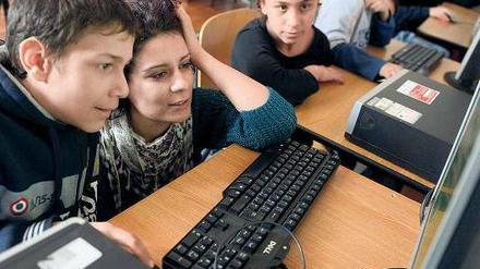 Kinder und Jugendliche und eine Lehrerin sitzen vor einer Reihe von Computern.