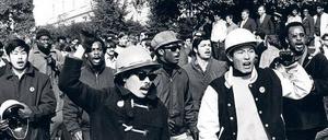 Schwarze und asiatische Studierende, die teilweise ihre geballten Fäuste erhoben haben, marschieren über den Campus einer Universität.