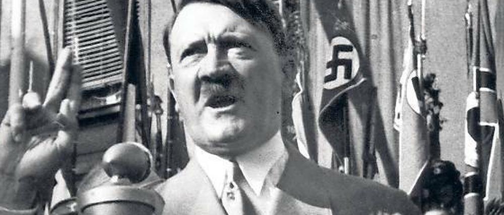 Adolf Hitler steht vor einem Mikrofon und spricht.