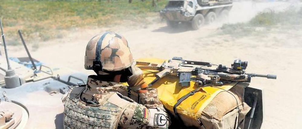 Ein Soldat steht in Uniform in der offenen Luke eines Panzers, vor ihm liegt ein Maschinengewehr.