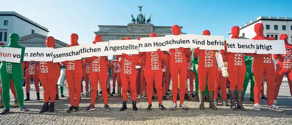 Menschen in roten Ganzkörperanzügen mit dem Schriftzug "befristet" stehen vor dem Brandenburger Tor.