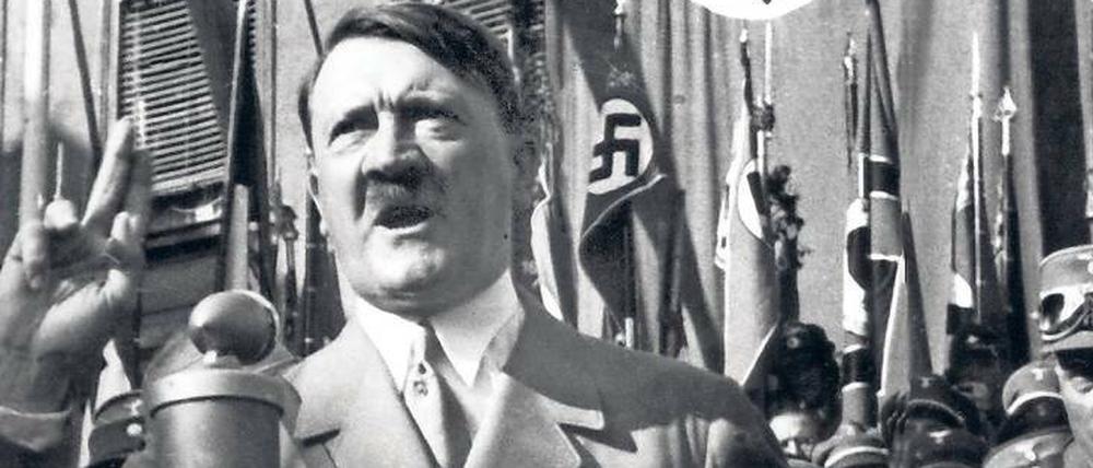Adolf Hitler steht an einem Mikrofon und spricht.