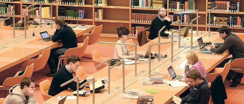 Junge Männer und Frauen sitzen in einer Bibliothek, lesen und arbeiten an ihren Laptops.