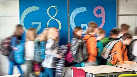 Schulkinder laufen vor einer Wandtafel von links nach rechts, auf der G8 und G9 geschrieben steht.