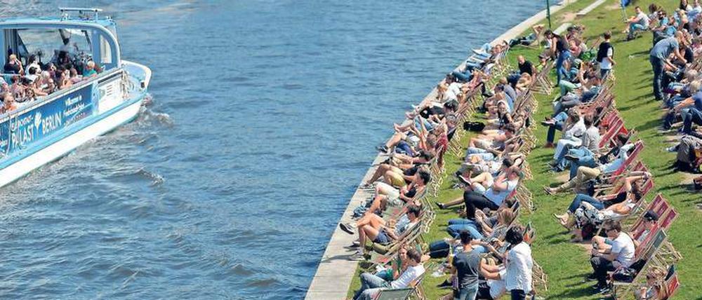 Menschen sitzen auf Liegestühlen an einem Flussufer.