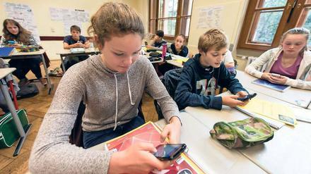 Schülerinnen und Schüler sitzen in einer Klasse und arbeiten mit ihren Smartphones.