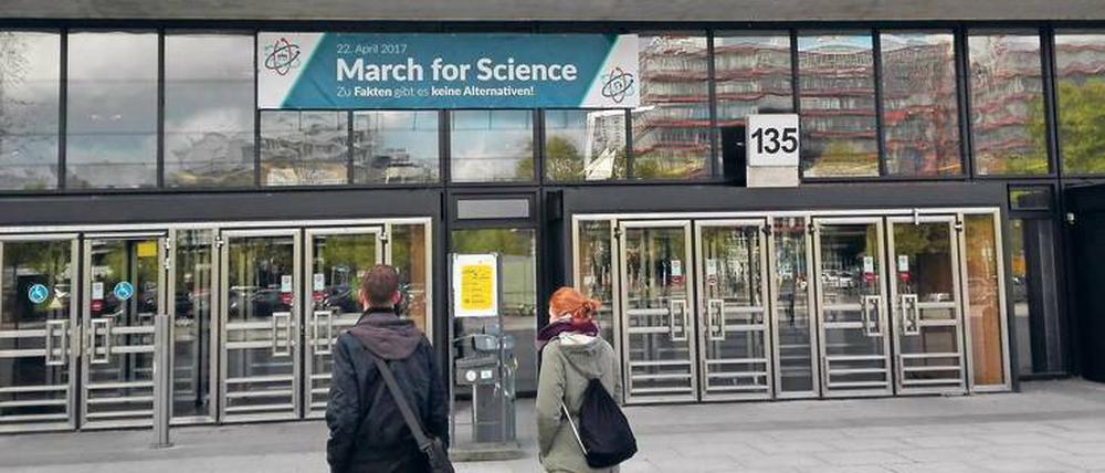 Zwei Studierende stehen vor der TU Berlin und blicken auf ein Plakat, das zum Science March aufruft.