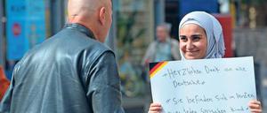 Eine Frau mit Kopftuch hält einem älteren Mann ein Schild entgegen, die Aufschrift besagt unter anderem: Herzlichen Dank an alle Deutsche.
