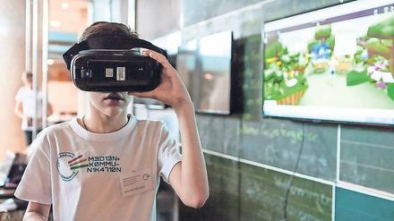 Ein Schulkind probiert im Klassenraum eine Virtual-Reality-Brille aus.