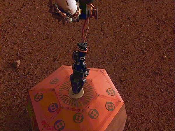 Das Seismometer SEIS, das hier gerade von dem Roboterarm neben dem Lander auf dem Marsboden abgesetzt wird, arbeitet zuverlässig.