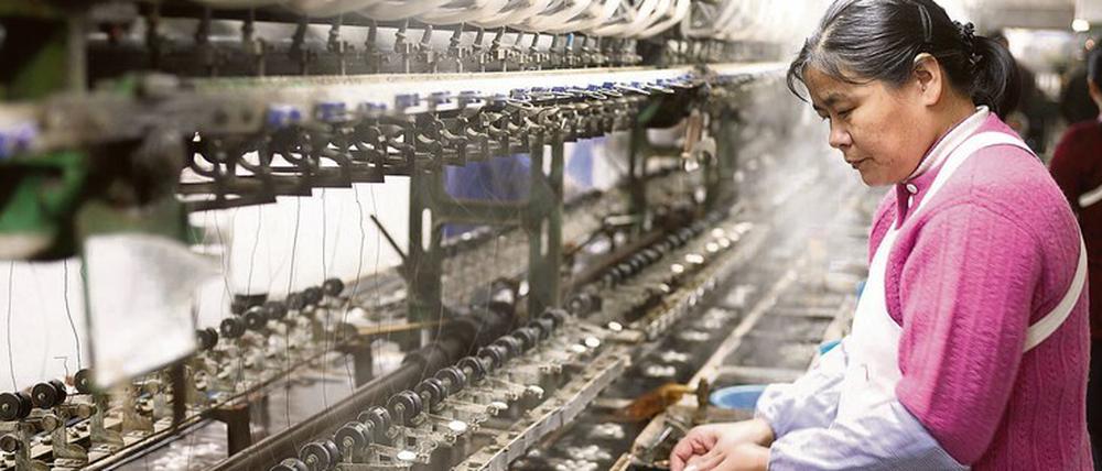 Eine Arbeiterin steht in einer chinesischen Seidenfabrik an einer Maschine, an der Seidenfäden gewonnen werden.