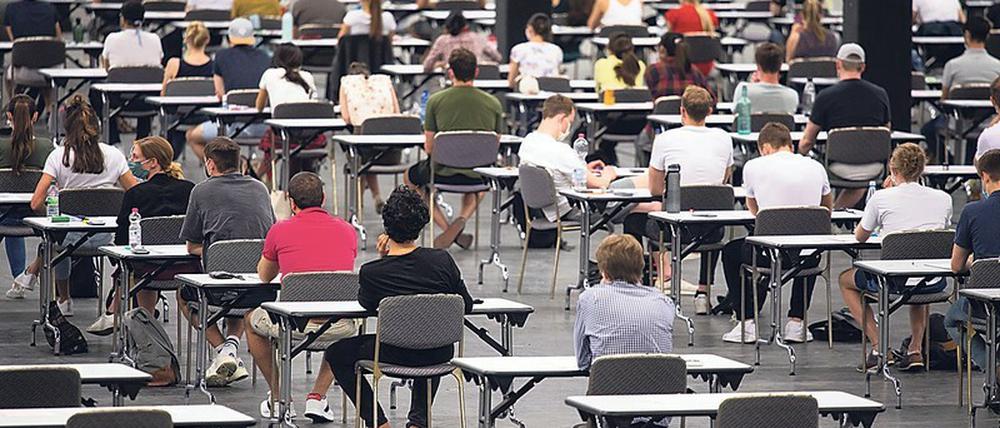 Studierende sitzen bei einer Prüfung in einer Messehalle an Einzeltischen.