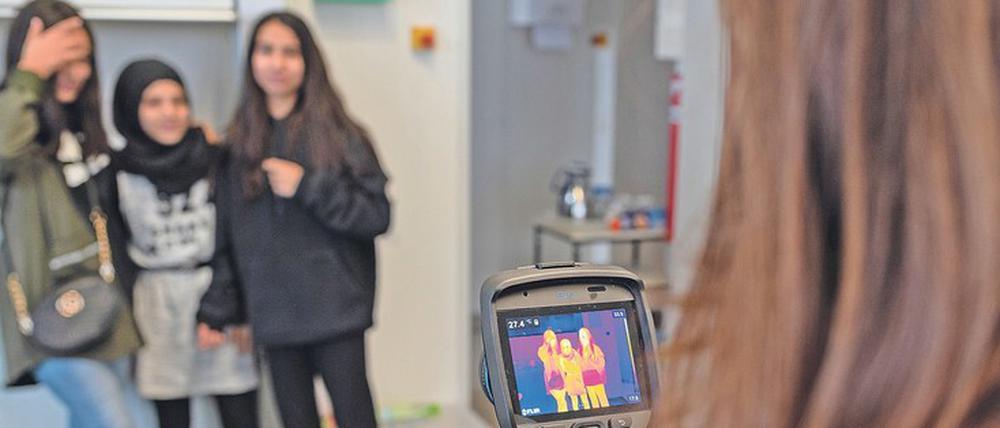 Eine Schülerin macht mit einer Wärmebildkamera eine Aufnahme von drei Mitschülerinnen.