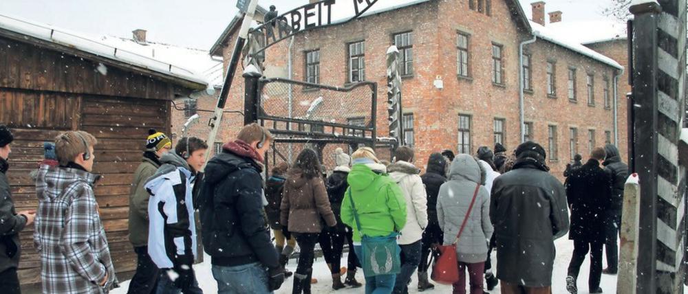 Eine Gruppe von Jugendlichen geht durch das Tor des ehemaligen Konzentrationslagers Auschwitz. Den Torbogen bildet der Schriftzug "Arbeit macht frei".